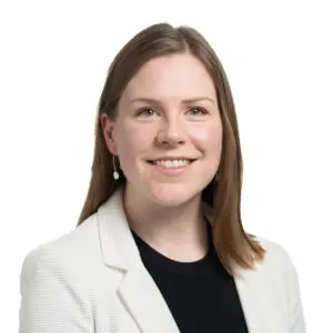 Dr Aoife Hunt, MBE, with straight brown hair, wearing a white blazer and black top, smiles at the camera against a plain white background in this 2024 portrait.