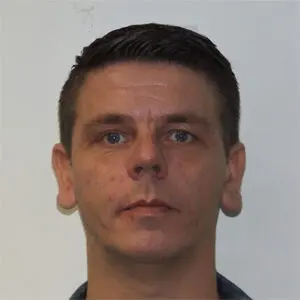 A man with short dark hair and blue eyes looks directly at the camera against a plain white background in this 2024 portrait of Stuart Doyle.