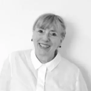 Stella Hall, a woman with fair hair and a fringe, wearing a collared white shirt, smiles at the camera against a plain white background.