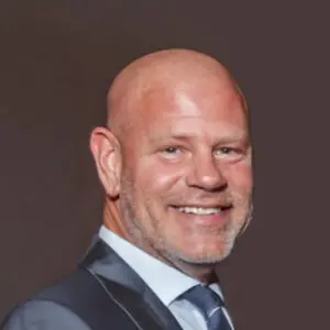 Smiling bald man in a suit and tie posed against a plain, dark background—Brian Dubiski, HS 2026.