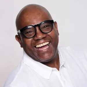 Bald man wearing glasses and a white shirt smiles broadly against a plain light background.