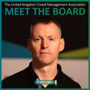 A man with short hair and a black shirt stands in front of a blurred background. Text reads The United Kingdom Crowd Management Association MEET THE BOARD and Board Members: Mark Logan.