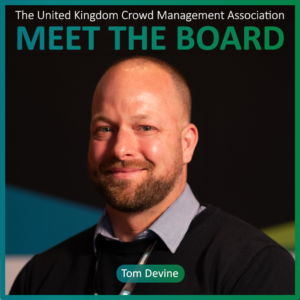 A man with a beard and bald head, wearing a dark jumper and collared shirt, smiles at the camera. Text reads MEET THE BOARD MEMBERS and Tom Devine, The United Kingdom Crowd Management Association.
